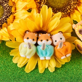 Three miniature Sylvanian Families hamster figures in green, teal, and orange outfits, posed on a sunflower surrounded by grass