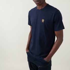 Model wearing Belstaff Phoenix Logo T-Shirt in Dark Ink, crew neck with gold phoenix chest logo, paired with dark trousers