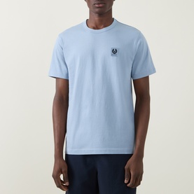 Model wearing Belstaff Phoenix Logo T-Shirt in mist blue, crew neck with embroidered chest logo, paired with navy trousers.