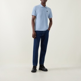 Model wearing Belstaff Phoenix Logo Polo Shirt in Mist Blue with dark wash jeans and black leather shoes.