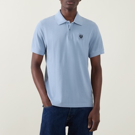 Model wearing Belstaff Phoenix Logo Polo Shirt in Mist Blue, featuring two-button placket and Phoenix logo badge, styled with dark jeans.