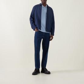 Model wearing Belstaff Phoenix Logo Polo Shirt in Mist Blue, styled with navy harrington jacket, dark indigo jeans and black leather shoes.