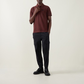 Model wearing Belstaff Phoenix Logo Tipped Polo Shirt in oxblood with contrast tipping, styled with dark cargo trousers and black boots.