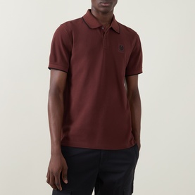 Model wearing Belstaff Phoenix Logo Tipped Polo Shirt in oxblood, with contrast tipping, short sleeves and Phoenix logo badge. Styled with navy