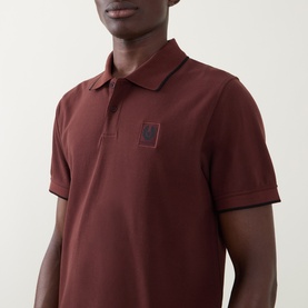 Model wearing Belstaff Phoenix Logo Tipped Polo Shirt in oxblood with contrast tipping, two-button placket, and Phoenix logo badge on chest.