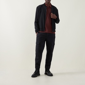 Model wearing Belstaff Phoenix Logo Tipped Polo Shirt in Oxblood, styled with black bomber jacket, cargo trousers and black boots.