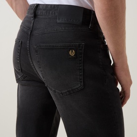 Model wearing Belstaff B69 Straight-Leg Jeans in Washed Black, showing rear pocket detail with gold logo badge and tonal stitching.
