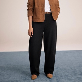 Model wearing Mint Velvet black wide-leg trousers, styled with a tan blazer, white tee, and tan heeled mules.