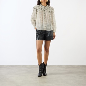 Model wearing Isabel Marant Etoile ecru and black printed cotton blouse with ruffle collar, styled with black leather shorts and western ankle boots.