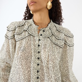 Model wearing Isabel Marant Etoile ecru and black spot-print cotton blouse with ruffle bib detail and button-through front, styled with gold hoop