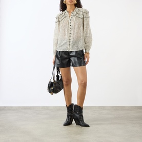 Model wearing Isabel Marant Etoile ecru and black cotton blend top with ruffle collar, styled with black leather shorts, boots and shoulder bag.