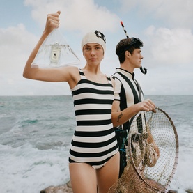 Jo Malone fragrance bottle held aloft by model in black and white striped swimsuit and white cap, coastal setting