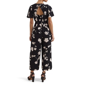 Model wearing Phase Eight black ivory floral jumpsuit with open tie back, short sleeves, and wide-leg cropped trousers, styled with block heel