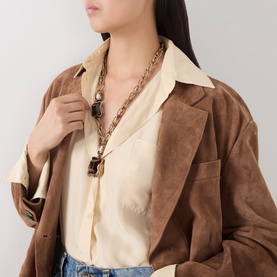 Model with chunky gold-tone chain necklace with dark pendant charms, styled with cream blouse and brown suede blazer