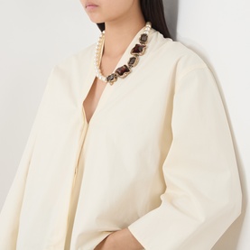 Model with pearl and dark stone statement necklace with gold-tone settings, styled with a cream oversized jacket