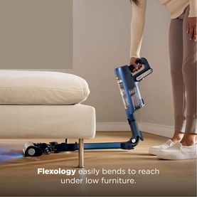 Shark PowerDetect Speed Clean and Empty Pet Pro Cordless Vacuum in blue, flexing under low sofa furniture demonstrating Flexology feature