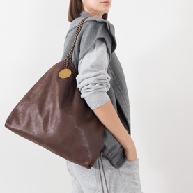 Model carrying Stella McCartney Falabella Drawstring Crossbody Bag in mahogany with gold chain strap and branded disc charm, styled with grey vest