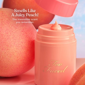 Too Faced Primed & Peachy Primer open jar with peach-toned cream texture, styled with fresh peaches and branded packaging in soft pink tones