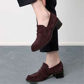 Model wearing Paul Green red suede penny loafers with block heel and brogue detailing, styled with dark cropped trousers