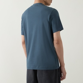 Model wearing Belstaff Alloy Logo T-Shirt in petrol, rear view showing crew neck, short sleeves and straight hemline, styled with dark grey trousers.