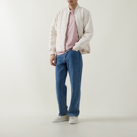 Model wearing Belstaff Border Logo Back Graphic T-Shirt in Dusk Pink, styled with cream bomber jacket, blue jeans and grey trainers.