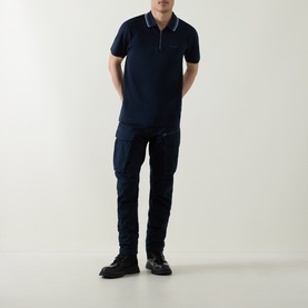 Model wearing Belstaff Alloy Logo Tipped Zip Polo Shirt in Dark Ink, styled with navy cargo trousers and black boots.