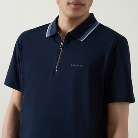 Model wearing Belstaff Alloy Logo Tipped Zip Polo Shirt in Dark Ink, featuring zip neckline, contrast tipped collar and short sleeves.