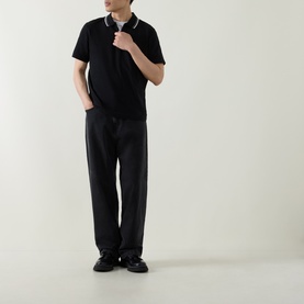 Model wearing Belstaff Alloy Logo Tipped Zip Polo Shirt in black with tipped collar, paired with dark trousers and black shoes.