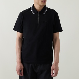 Model wearing Belstaff Alloy Logo Tipped Zip Polo Shirt in black with white tipped collar trim and zip neckline, styled with black shorts.