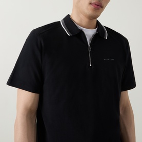 Model wearing Belstaff Alloy Logo Tipped Zip Polo Shirt in black with white tipped collar trim and zip neckline, short sleeves.