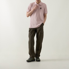 Model wearing Belstaff Logo Badge Polo Shirt in Dusk Pink with logo patch, styled with dark khaki cargo trousers and black shoes.