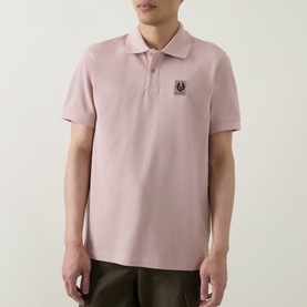 Model wearing Belstaff Logo Badge Polo Shirt in Dusk Pink, short sleeves, polo collar, logo patch detail, styled with khaki trousers.