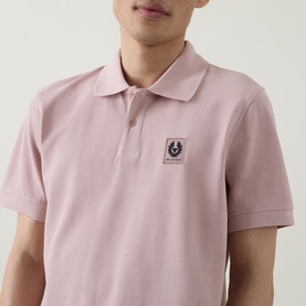 Model wearing Belstaff Logo Badge Polo Shirt in Dusk Pink, showing logo patch detail on chest, polo collar and short sleeves.
