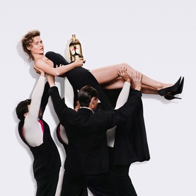 Jean Paul Gaultier La Favorite Eau de Parfum gold bottle held aloft in a dramatic fashion campaign scene with models in black outfits