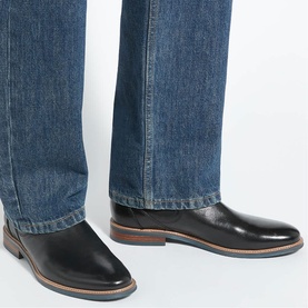 Model wearing black leather oxford shoes with brown layered sole, styled with mid-wash blue jeans
