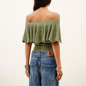 Model wearing Bash green off-shoulder ruffle crop top, styled with wide-leg denim jeans and silver bracelets, back view