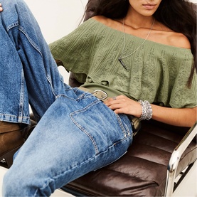 Model wearing Bash green off-shoulder knit top with blue denim jeans, styled with silver layered necklace and stacked bracelets