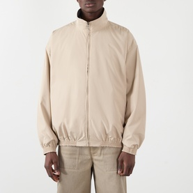 Model wearing Acne Reversible Logo Jacket in beige, high collar, front zip fastening, elasticated cuffs, styled with beige trousers