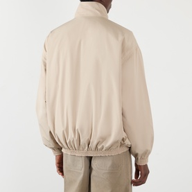 Model wearing Acne Reversible Logo Jacket in beige, rear view showing dropped shoulders, elasticated hem and cuffs, styled with beige trousers