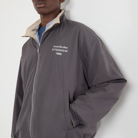 Model wearing Acne Reversible Logo Jacket in beige, showing grey side with white Stockholm 1996 chest logo print and high collar