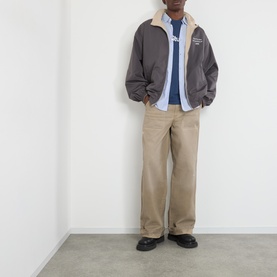 Model wearing Acne Reversible Logo Jacket in beige, styled with light blue shirt, khaki trousers and black loafers.