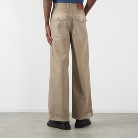 Model wearing Acne Stained Twill Trousers in camel beige, wide-leg with upturned hems and rear patch pockets visible from behind.