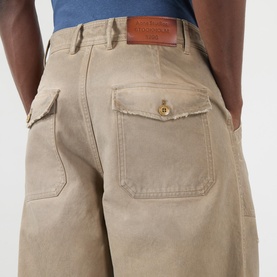 Model wearing Acne Stained Twill Trousers in camel beige, showing rear patch pocket with raw edge detailing and leather logo patch.