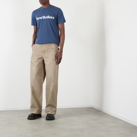Model wearing Acne Graphic Logo T-Shirt in navy with crew neck, styled with beige wide-leg trousers and black loafers.