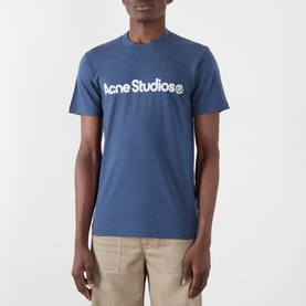 Model wearing Acne Graphic Logo T-Shirt in navy, crew neck with white logo print across chest, styled with beige trousers
