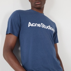 Model wearing Acne Graphic Logo T-Shirt in navy, featuring white chest logo print and crew neckline, cropped close-up view.