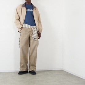 Model wearing Acne Graphic Logo T-Shirt in navy, styled with a beige jacket, wide-leg chinos and a striped shirt tied at the waist.