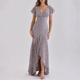 Model wearing House of CB Lilac Vintage Floral maxi dress with flutter sleeves, V-neck tie detail, and asymmetric ruffle hem.