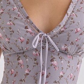 Model wearing House of CB Lilac Vintage Floral top with V-neckline, ribbon tie detail and lace trim, pink floral print on grey fabric.