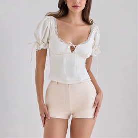 Model wearing House of CB ivory puff-sleeve crop top with sweetheart neckline and tie detail, styled with beige mini shorts.